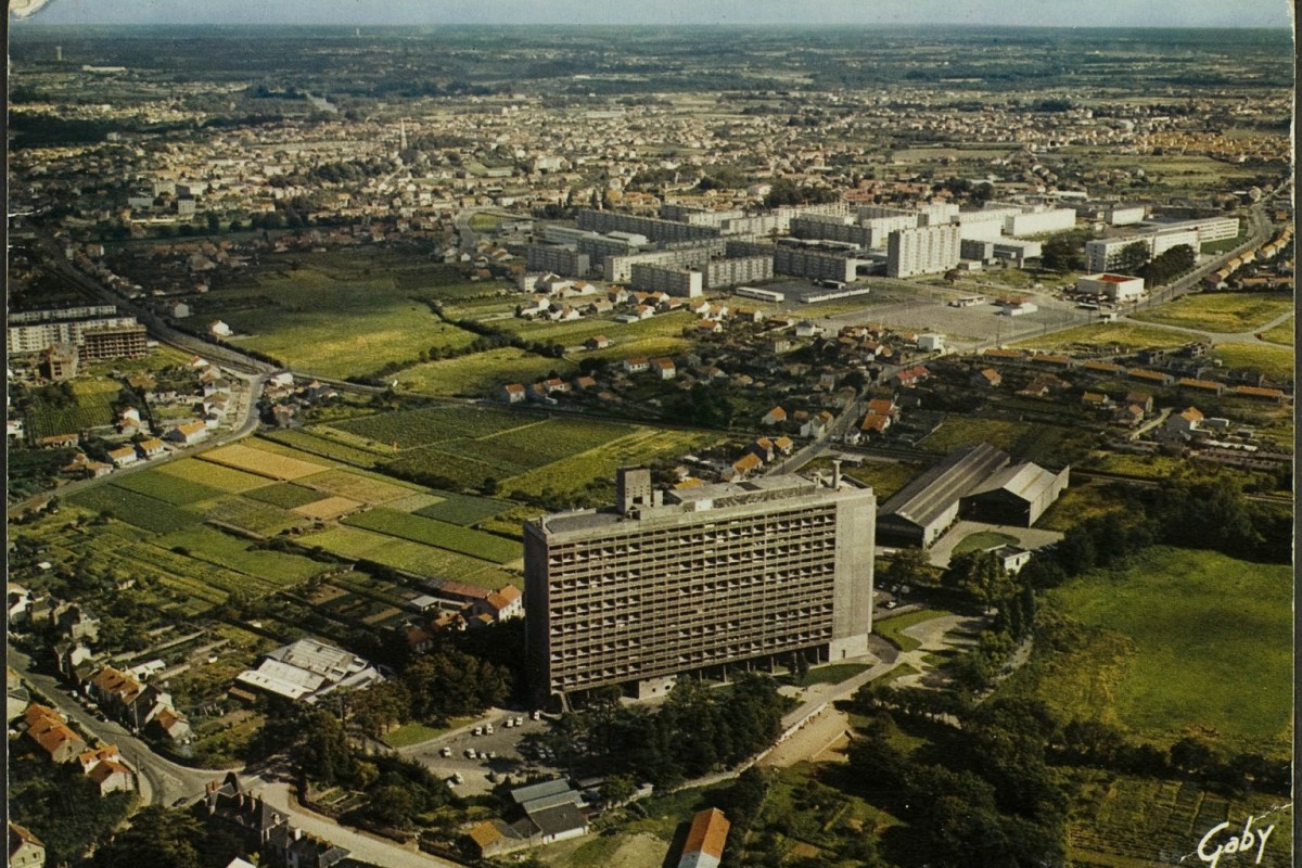 Vue aérienne de La Maison Radieuse, côté Nord-Ouest ; château de la Bouvardière, boulevard Le Corbusier, rue Georges Boutin, rue Théodore Brosseaud, quartier de Mauperthuis, des Mahaudières et du Château, église Saint-André, rue Victor Hugo, clocher de l'église Saint-Paul et quartier Saint-Paul et des Trois-Moulins en arrière-plan