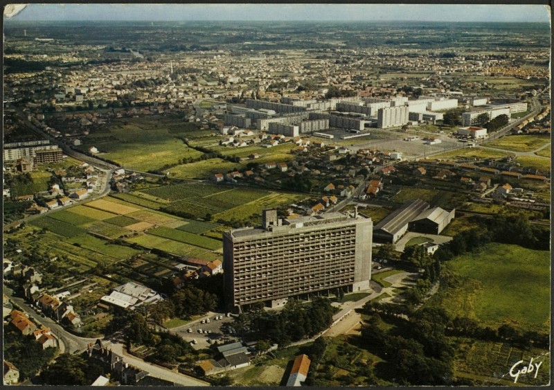 Vue aérienne de La Maison Radieuse, côté Nord-Ouest ; château de la Bouvardière, boulevard Le Corbusier, rue Georges Boutin, rue Théodore Brosseaud, quartier de Mauperthuis, des Mahaudières et du Château, église Saint-André, rue Victor Hugo, clocher de l'église Saint-Paul et quartier Saint-Paul et des Trois-Moulins en arrière-plan